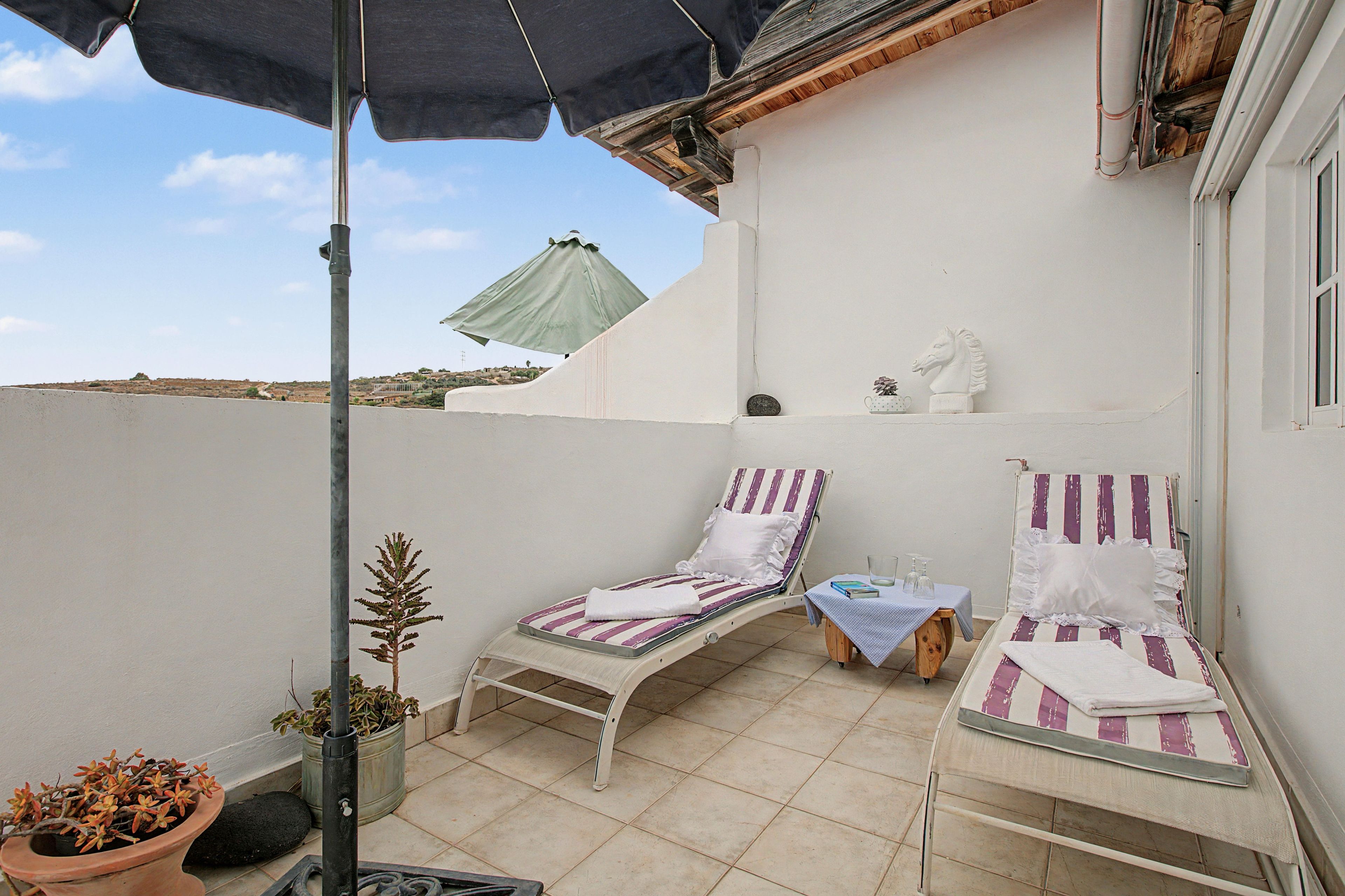 Een klein balkon buiten met twee ligbedden, een potplant en een decoratief paardenhoofd.
