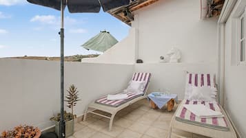 Een klein balkon buiten met twee ligbedden, een potplant en een decoratief paardenhoofd.