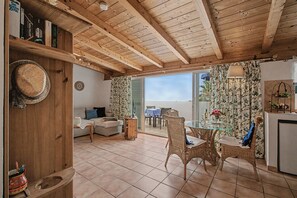Un interior acogedor con techo de madera, una zona de comedor con sillas de mimbre, un sofá y una cocina con refrigerador.