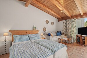 Une chambre à coucher comprenant un lit, des tables de chevet, un canapé, une télévision et une fenêtre avec des rideaux.