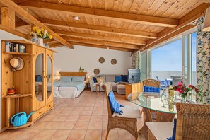 A cozy room with a wooden ceiling, a bed with blue bedding, a sofa, a dining table with chairs, and a large window. - Holiday Apartment for 3 People (54 m²) in La Sabinita (La Sabinita)