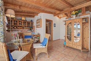 Un interior rústico con vigas de madera, un comedor con mobiliario de mimbre y una cocina con armarios de madera.