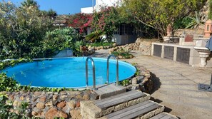 A swimming pool with a wooden deck and stone steps leading to it, surrounded by lush greenery and a stone wall. - Holiday Apartment for 3 People (54 m²) in La Sabinita (La Sabinita)