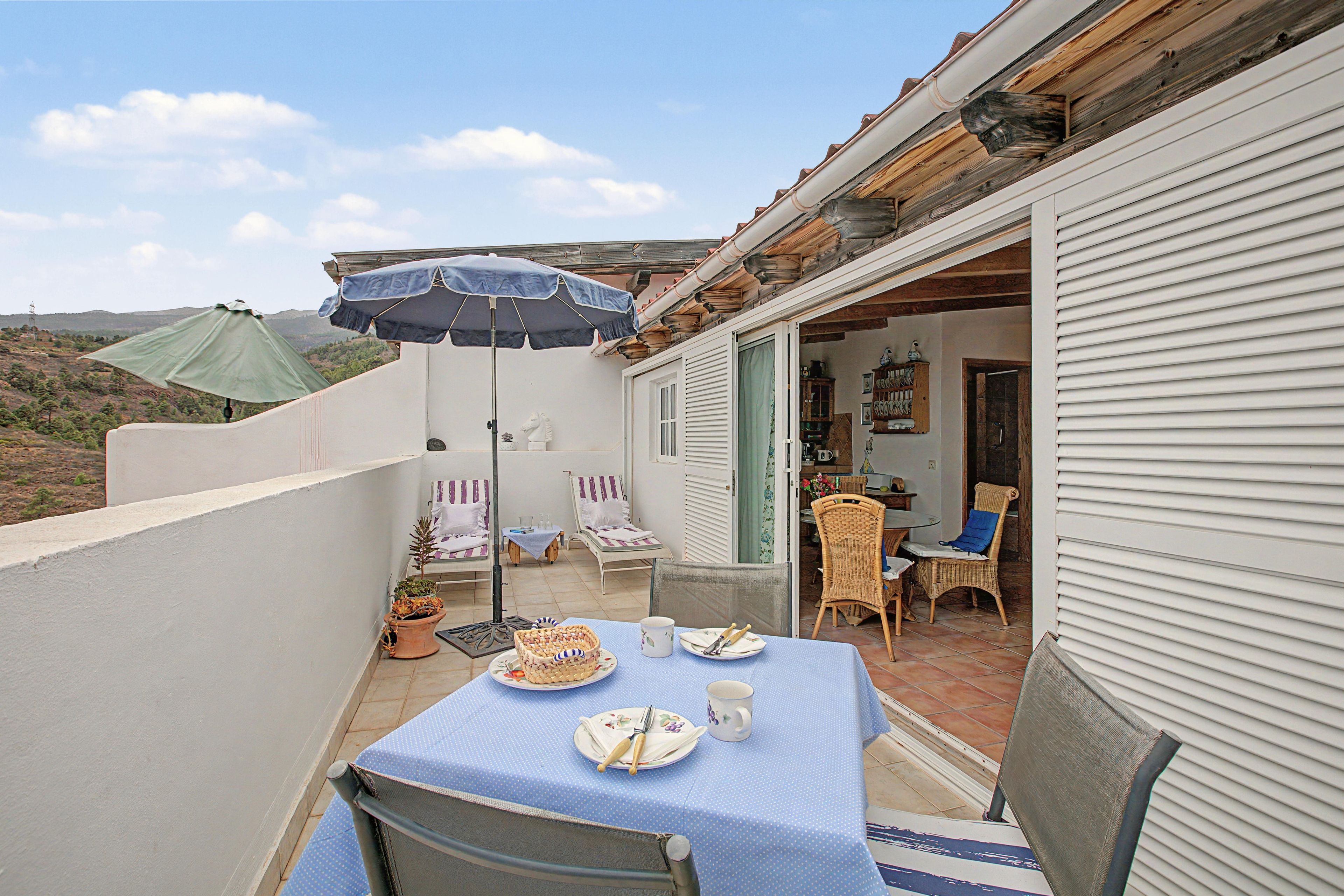 A patio with a table set for dining, two lounge chairs, a wicker chair, and a small table with a green umbrella.