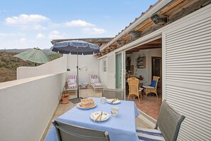 Un patio con una mesa lista para comer, dos sillones de descanso, una silla de mimbre y una pequeña mesa con un parasol verde.