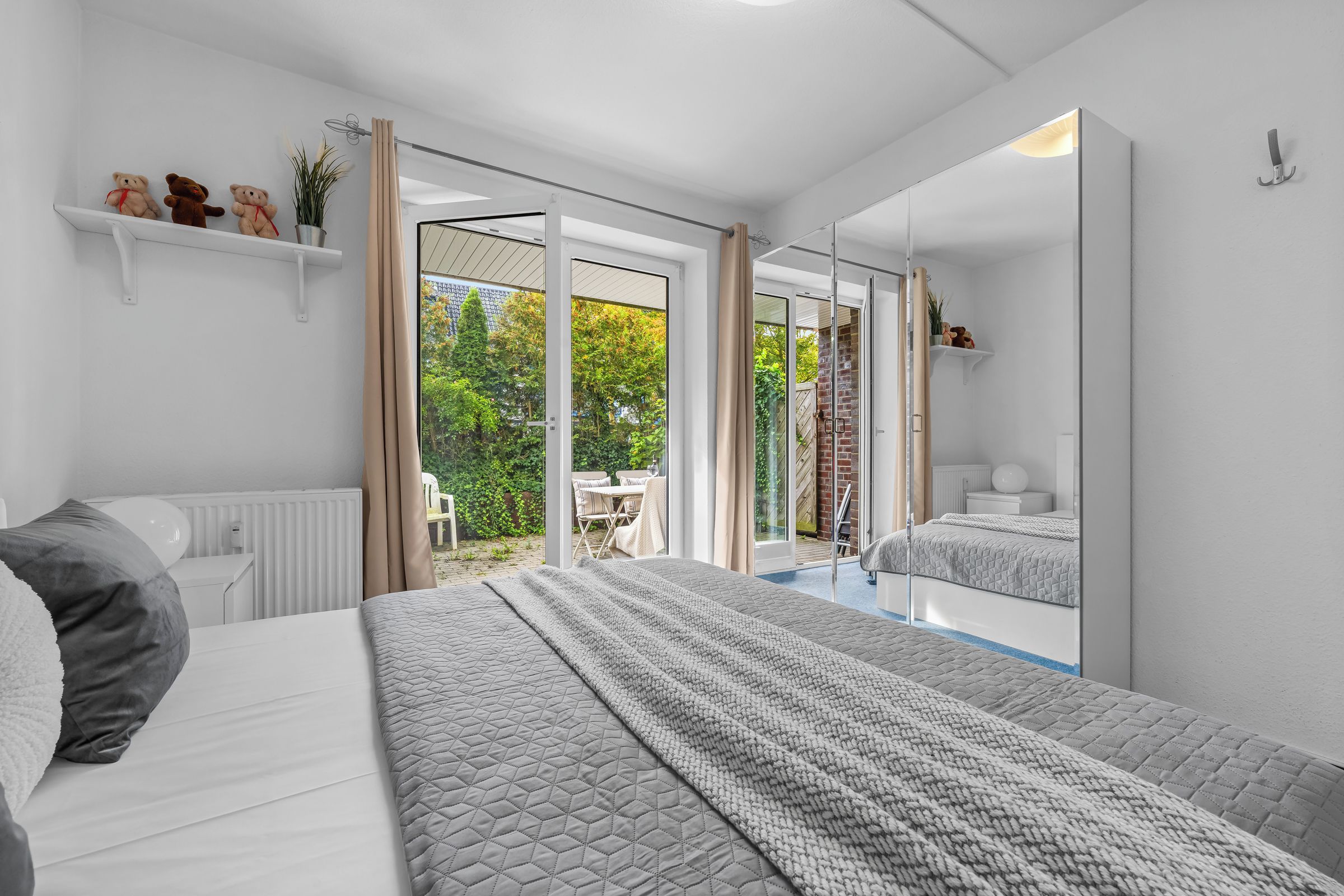 Een slaapkamer met een groot bed, een nachtkastje, een spiegel en uitzicht op de tuin.