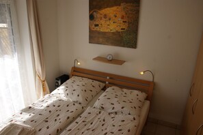 Ein Schlafzimmer mit einem hölzernen Bett, zwei Kissen, einem Nachttisch mit einer Uhr und einem Bild an der Wand.