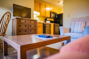 A living room with a wooden coffee table, a television on the wall, and a kitchen in the background. - Pigeon Forge | Smoky Mountain Villa | Spa + Pool (Pigeon Forge)