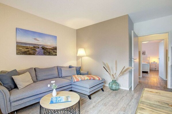 Una sala de estar moderna con un sofá seccional gris, una mesa de centro redonda y un cuadro con una escena de playa.