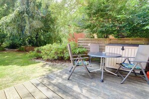 Un patio exterior con terraza de madera, una mesa redonda, dos sillas y una parrilla de barbacoa integrada.
