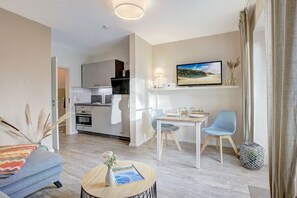 A modern living room with a sofa, a coffee table, and a dining area with a table and chairs. - Holiday apartment with 1 bedroom (St. Peter-Ording)