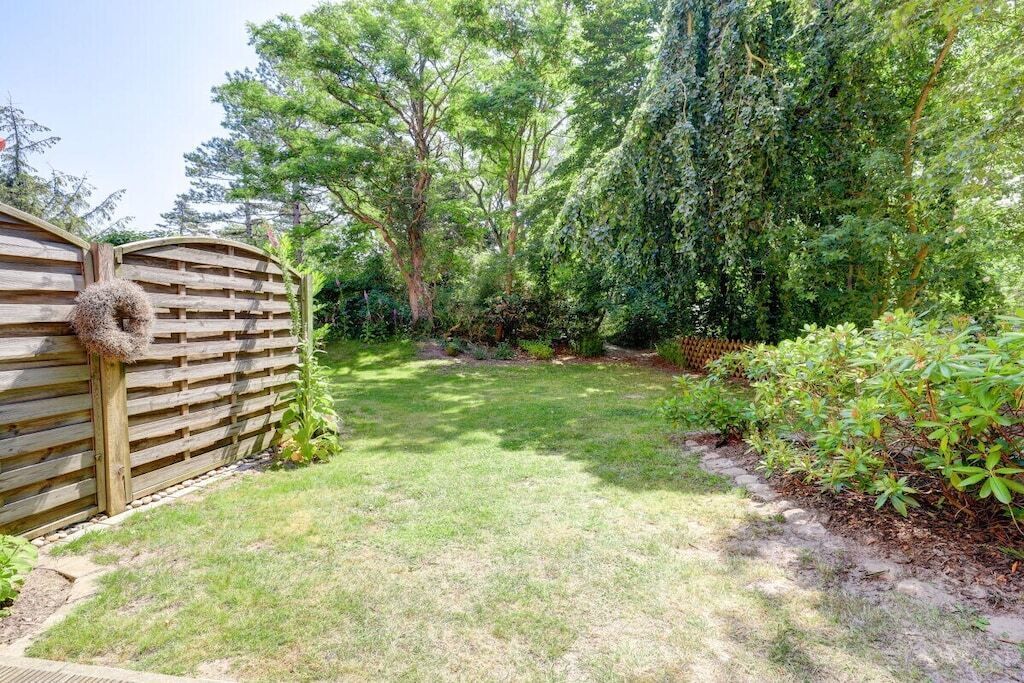 Ein umzäunter Garten mit Holztor, Rasen und verschiedenen Sträuchern und Bäumen.