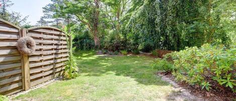 Ein umzäunter Garten mit Holztor, Rasen und verschiedenen Sträuchern und Bäumen.