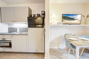 A modern kitchen with a built-in oven, microwave, and coffee maker. There is a dining area with a wooden table and chairs. - Holiday apartment with 1 bedroom (St. Peter-Ording)