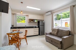 A compact living space with a kitchenette, dining area, sofa, and large windows. - Modern in Condo w/ Parking in Rio Tavares Ala0001 (Florianópolis)