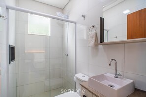 A modern bathroom with a glass shower enclosure, a white sink, and a wooden vanity. - Modern in Condo w/ Parking in Rio Tavares Ala0001 (Florianópolis)