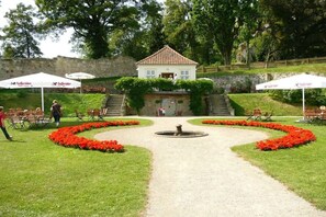 A garden with a central fountain, a white building with a red roof, and outdoor seating areas. - Holiday apartment Assenta (Blankenburg)