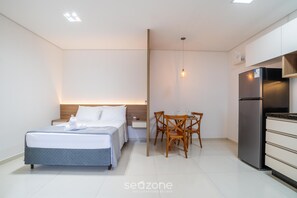 Ein modernes Hotelzimmer mit Bett, Nachttisch, einem kleinen Esstisch mit Stühlen, einem Kühlschrank und einer Pendelleuchte.