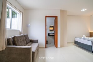 Ein Hotelzimmer mit Sofa, Bett, Badezimmer mit Spiegel und Blick durch eine geöffnete Tür.