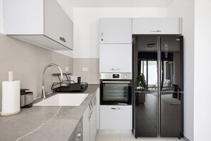 A modern kitchen with a built-in oven, a stainless steel refrigerator, and a sleek faucet. - Cozy & Spacious 3BR with Balcony & Mamad (Bat Yam)