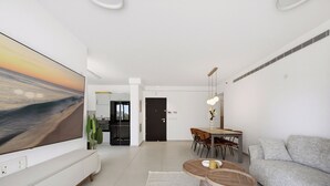 Un saló modern amb televisió plana, un sofà, una taula de dinar amb cadires i una cuina al fons.