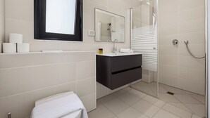 Bany modern amb vàter, rentapel, mirall i plat de dutxa.
