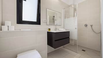 Un baño moderno con inodoro, lavamanos, espejo y ducha.