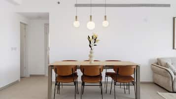 Un comedor con una mesa rectangular, cuatro sillas, un florero con flores y luces colgantes.