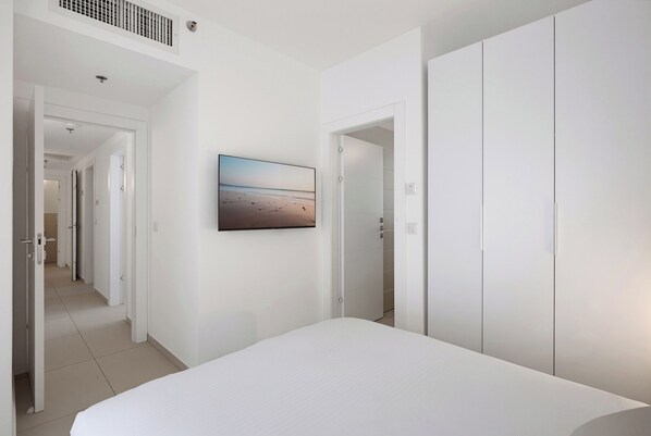 A bedroom with a bed, a television mounted on the wall, and a wardrobe. - Cozy & Spacious 3BR with Balcony & Mamad (Bat Yam)