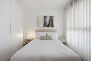 A hotel room with a large bed, a bedside table with a lamp, a nightstand, and a painting on the wall. - Cozy & Spacious 3BR with Balcony & Mamad (Bat Yam)