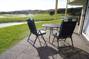 Une terrasse extérieure avec deux chaises et une table, un chemin pavé et une vue sur une route et des champs verdoyants.
