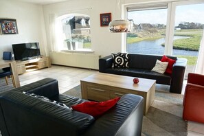 A living room with a sofa, a coffee table, a television, and a view of a river. - Residence Juliana 45 (Julianadorp)