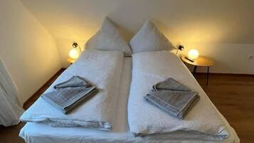 A twin bed with pillows and a blanket, two bedside lamps, and a wooden floor.