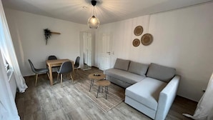 A modern living room with a sofa, a dining table with chairs, and a hanging light fixture.