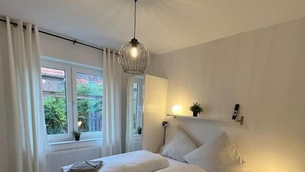 A bedroom with a double bed, bedside tables, a hanging light fixture, and a window with curtains.