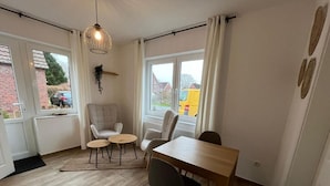 A room with a dining table, chairs, a hanging light fixture, and a view through a window.