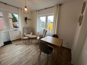 Une pièce comprenant une table à manger, des chaises, un luminaire suspendu et une vue par la fenêtre.