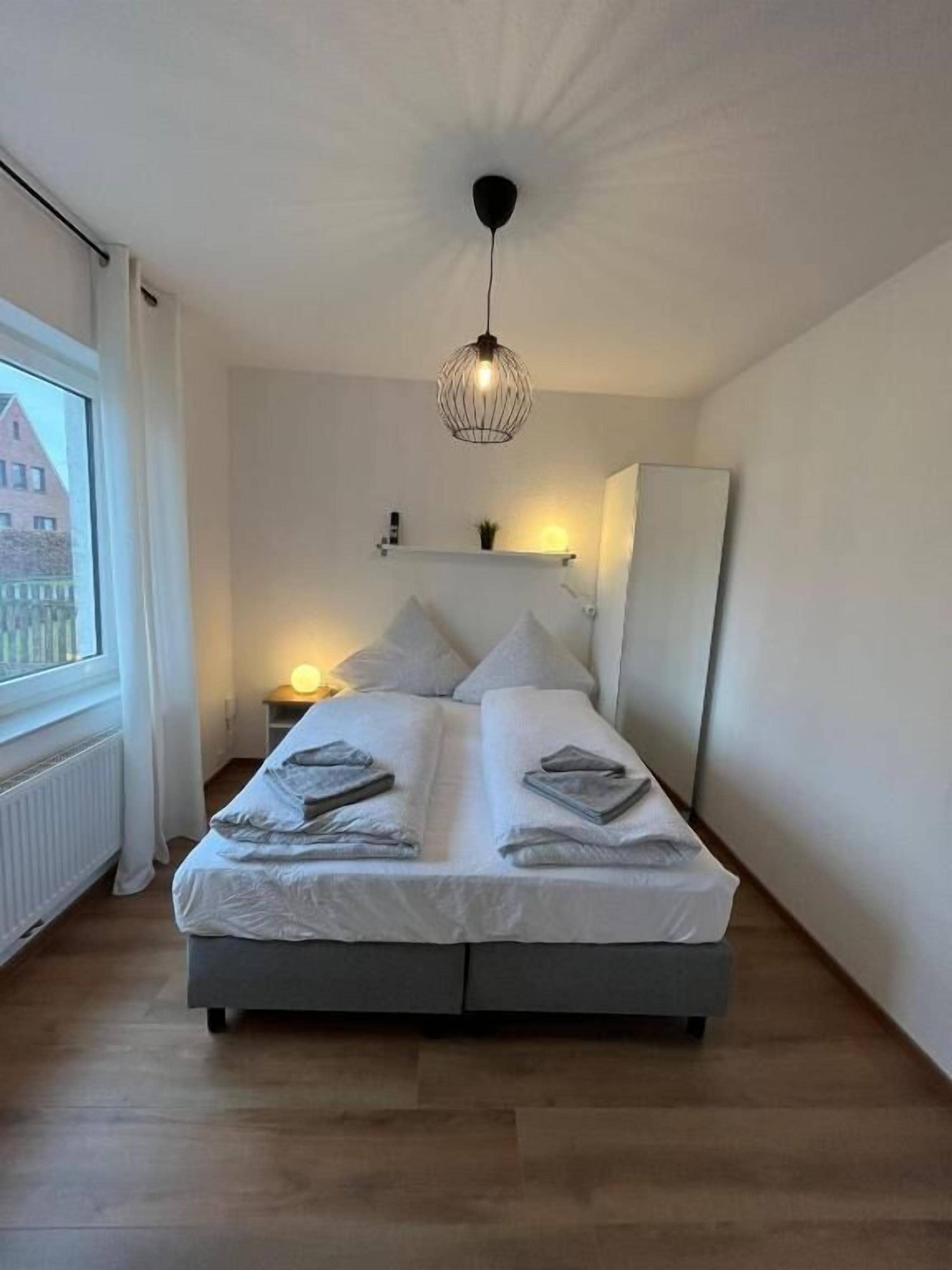 Un dormitorio con una cama, mesitas de noche, una lámpara colgante y una ventana con vistas.
