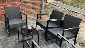 An outdoor patio with a brick wall, a red door, and a metal table with four chairs. - Ostfriesenperle (Aurich)
