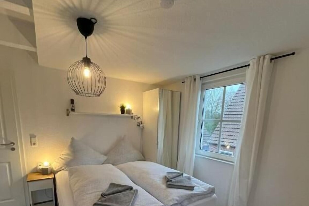 Une chambre à coucher avec un lit, une table de chevet, une lampe et une fenêtre.