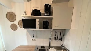 A compact kitchen with a microwave, coffee maker, and utensils hanging on the wall.