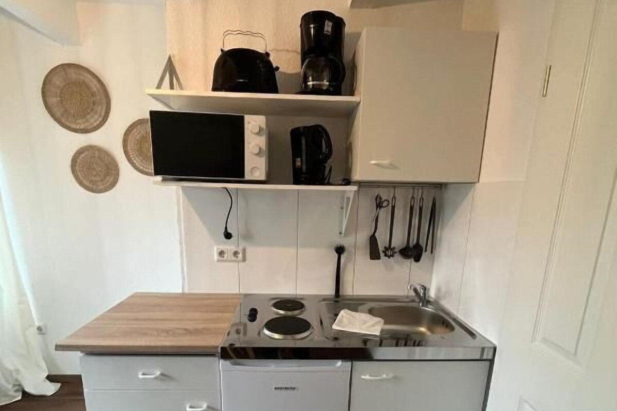 Une cuisine compacte équipée d’un four à micro-ondes, d’une machine à café et d’ustensiles de cuisine accrochés au mur.