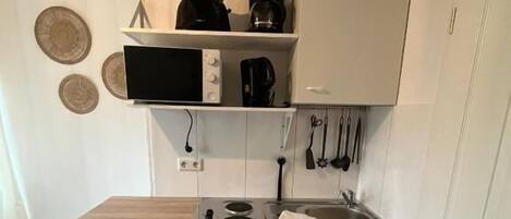 Cocina compacta con microondas, cafetera y utensilios colgados en la pared.