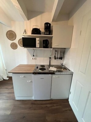 Une cuisine compacte équipée d’un four à micro-ondes, d’une machine à café et d’ustensiles de cuisine accrochés au mur.