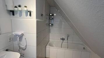 Ein Badezimmer mit einem weißen Waschbecken, einer Badewanne und einer Dusche. Es gibt Regale mit Pflanzen sowie einen Handtuchhalter.