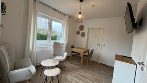 A modern kitchen with a dining area, including a table and chairs, a refrigerator, and a window with curtains. - Ostfriesenperle (Aurich)