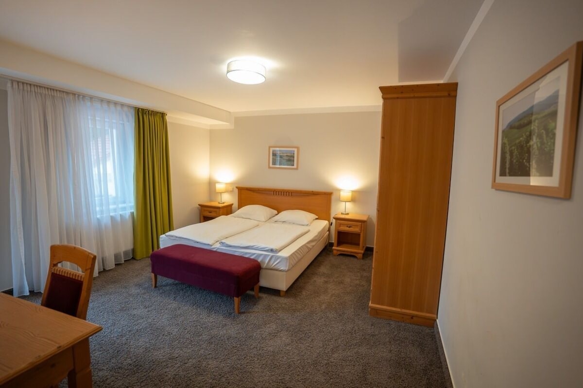Habitación de hotel con cama, mesitas de noche, una silla, un escritorio y un cuadro en la pared.