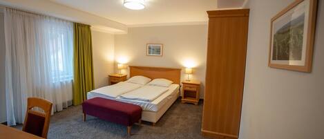 Quarto de hotel com cama, mesas de cabeceira, uma cadeira, escrivaninha e um quadro na parede.