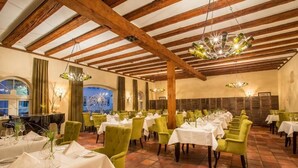 A restaurant with multiple tables set for dining, wooden beams on the ceiling, and a piano in the background.