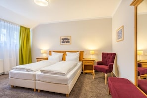 Habitación de hotel con cama doble, dos mesitas de noche con lámparas, un sillón rojo, un banco y un espejo grande.